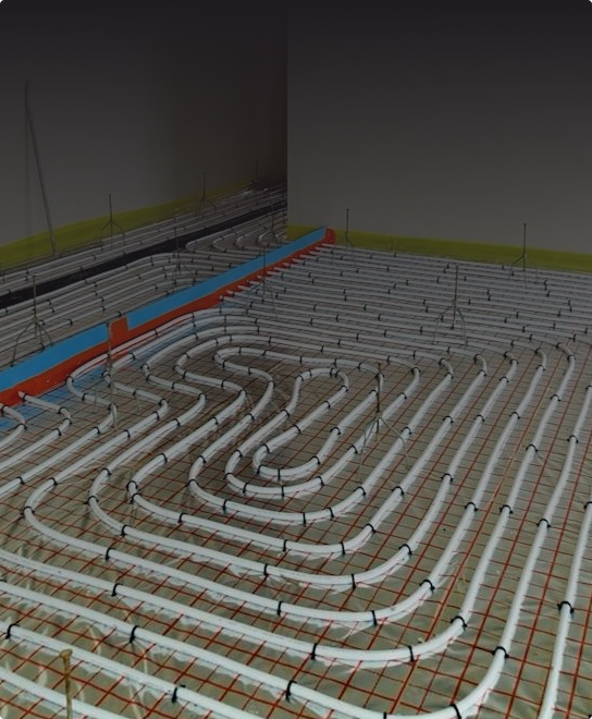 Białe rury ułożone w kratkę do ogrzewania podłogowego są instalowane na betonowej podłodze, zabezpieczone klipsami i siatką, w niedokończonym pomieszczeniu.