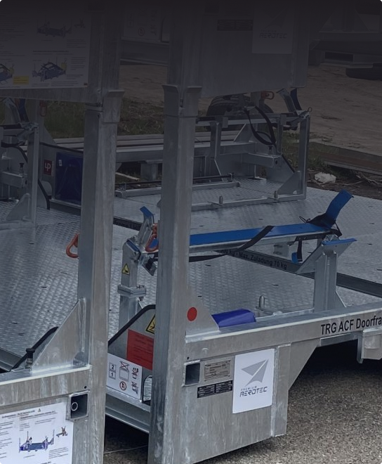 Widok z bliska metalowych platform sprzętowych z niebieskimi pasami i etykietami ostrzegawczymi, ustawionych na zewnątrz, na utwardzonej powierzchni.