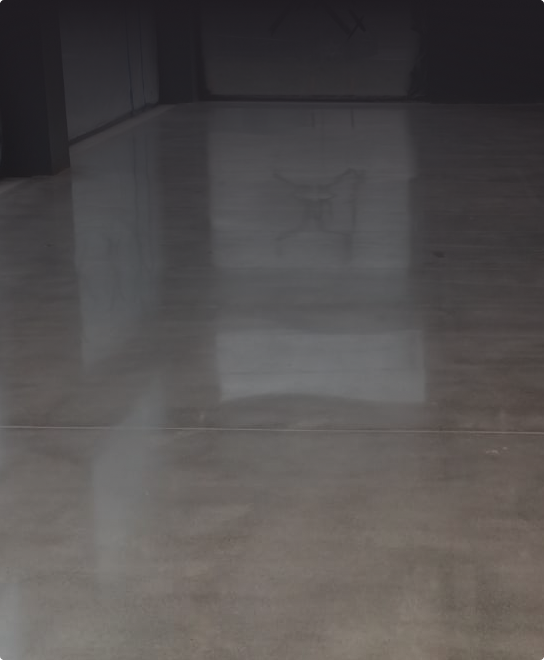 Gładka, polerowana betonowa podłoga, w której odbijają się kontury okien i wentylator sufitowy nad nią.