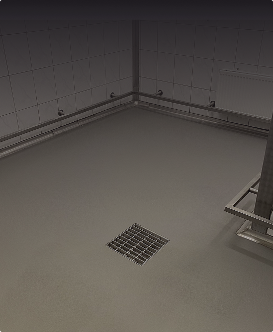 Czysty, pusty, wyłożony kafelkami pokój z metalowym odpływem podłogowym pośrodku, metalowymi poręczami wzdłuż ścian i białym grzejnikiem zamontowanym na ścianie.